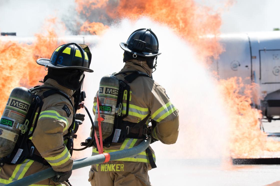 Two firefighters spraying fire retardant on a fire training aircraft during an exercise